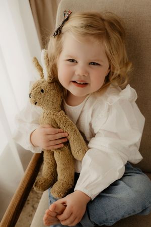 A child snuggles their favorite plush bunny while sitting in a cozy beige chair.