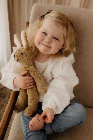 A child in white dress and jeans cuddles with their plush bunny on a beige armchair.