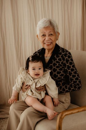 Family portrait showing loving embrace between generations against neutral backdrop.