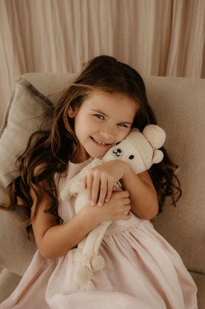 Young child hugs teddy bear while relaxing on beige couch.