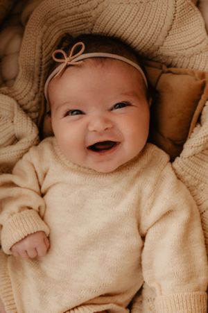 Joyful baby wearing cream sweater and bow headband while smiling.