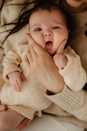 Baby wearing cream sweater making playful expression while being held.