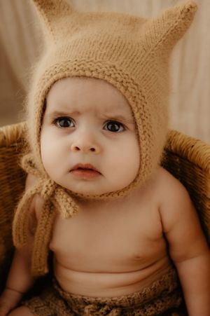 Close-up portrait of baby wearing knit bear bonnet with expressive eyes in sepia tones.