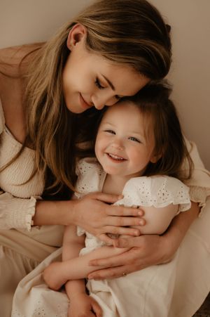 Mother and daughter sharing joyful cuddles in matching white outfits.