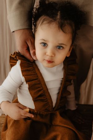 Baby in brown overalls and white turtleneck shows bright expressions.