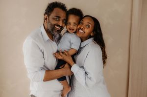 Family shares loving embrace and laughter in casual white button-down shirts.