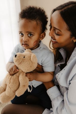 Family cuddles together while holding soft beige teddy bear in intimate portrait.