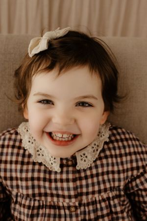 Charming portrait of a child wearing a gingham dress with lace collar and white hair bow.