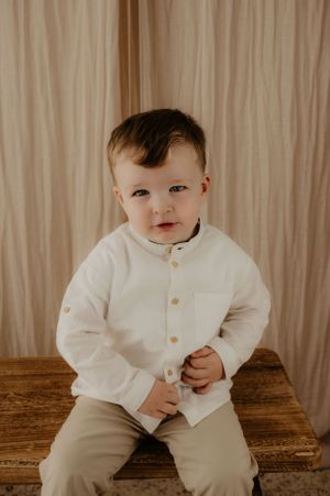 Child in white button-up shirt sitting on wooden surface.