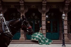 Woman in green gown poses beside dark horses in front of ornate building with teal doors. Charleston, Summerville,South Carolina