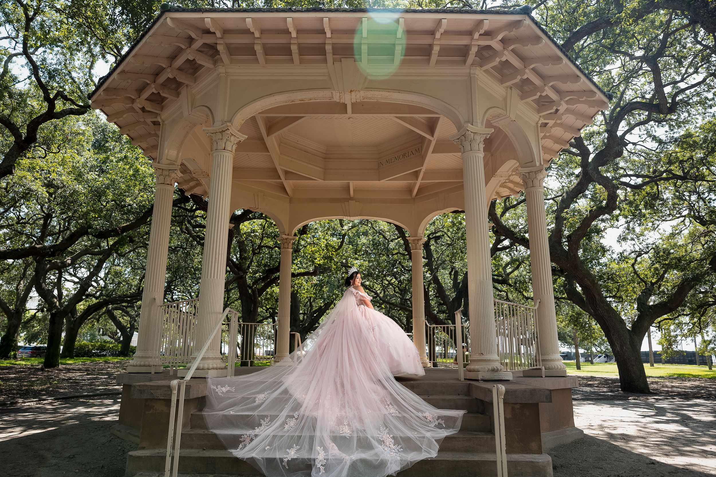A QUINCEAñERA in a flowing pink ball gown poses under an elegant white gazebo surrounded by oak trees in a lush park.
Charleston, sc