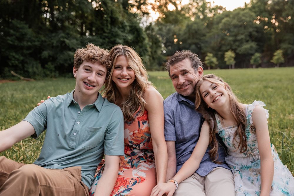 Family of four smiling and sitting together on green grass in a sunny park during golden hour.