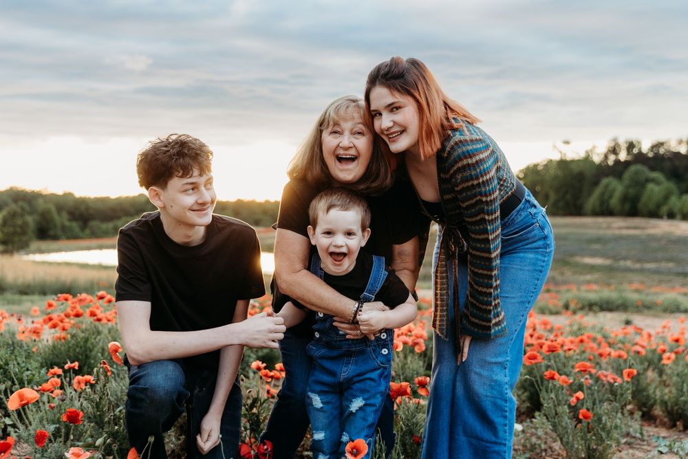 Family of four laughing together in a vibrant poppy field at sunset, with a toddler in denim overalls.