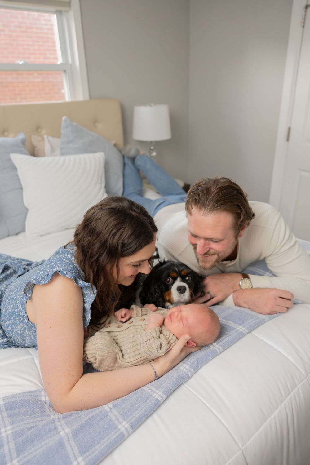 A couple lies together on a bed with their small dog and newborn baby sharing a moment in their royal oak Michigan home.
