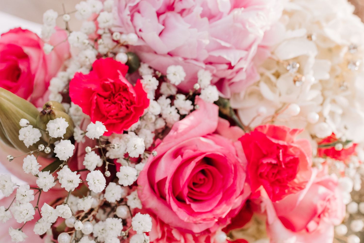 Close-up of a bridal bouquet featuring pink roses, peonies, carnations, and white baby's breath.
