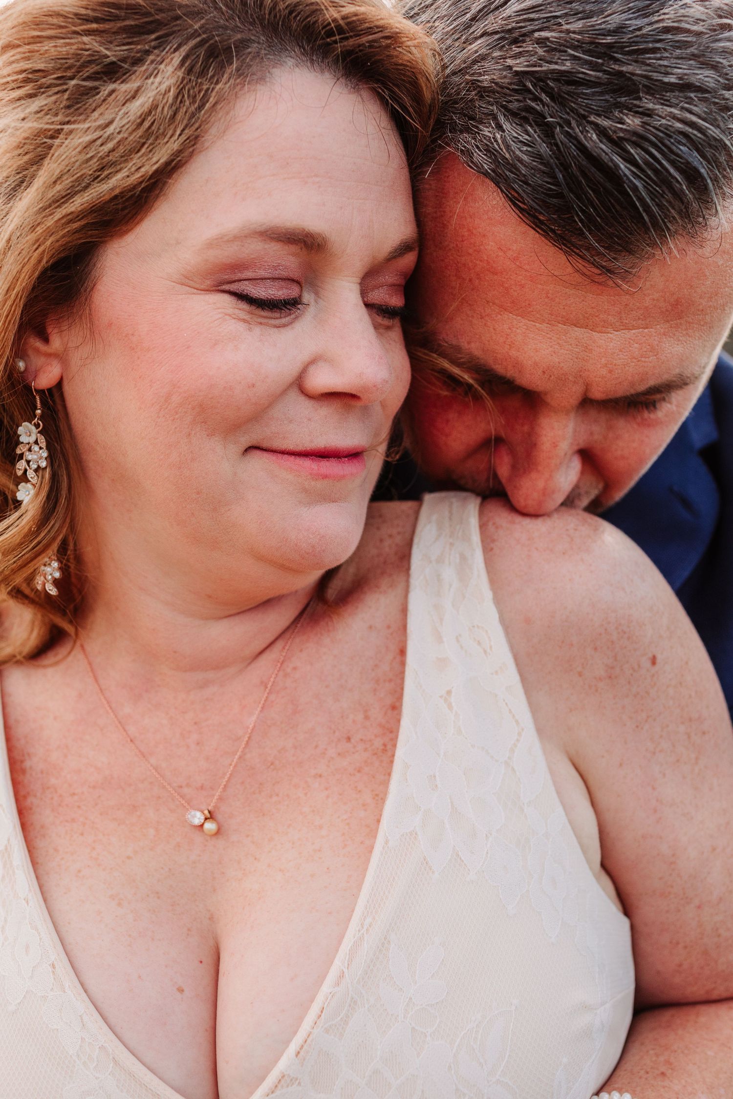 Intimate close-up of bride and groom, groom nuzzling bride tenderly in warm golden light.