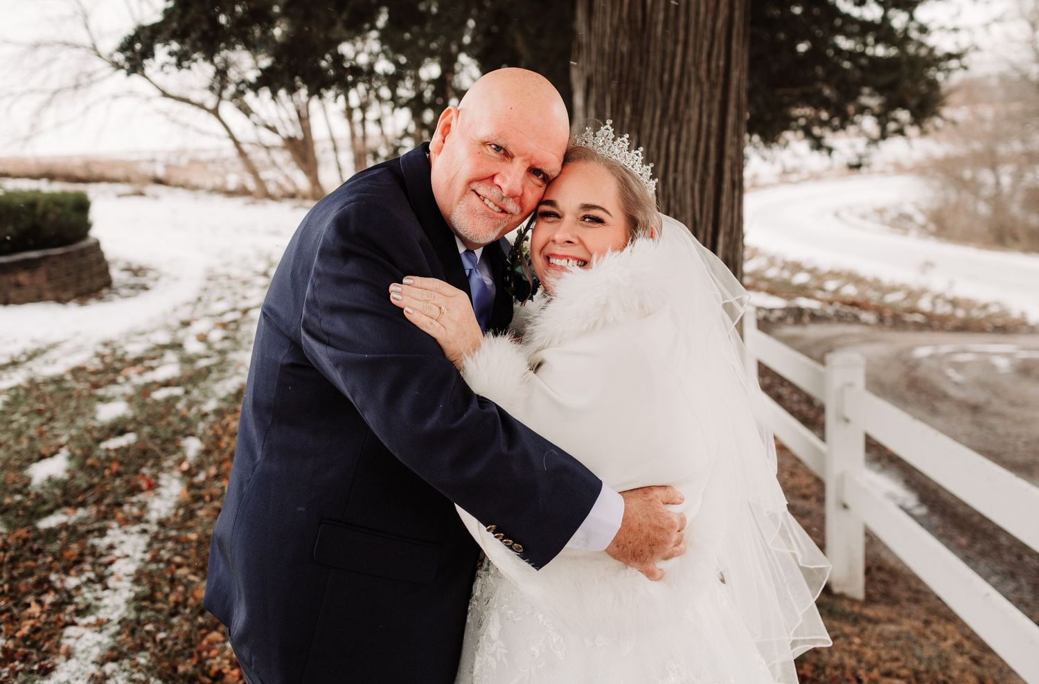 Bride and groom embracing outdoors in winter snow, bride wearing white gown and crown veil.
