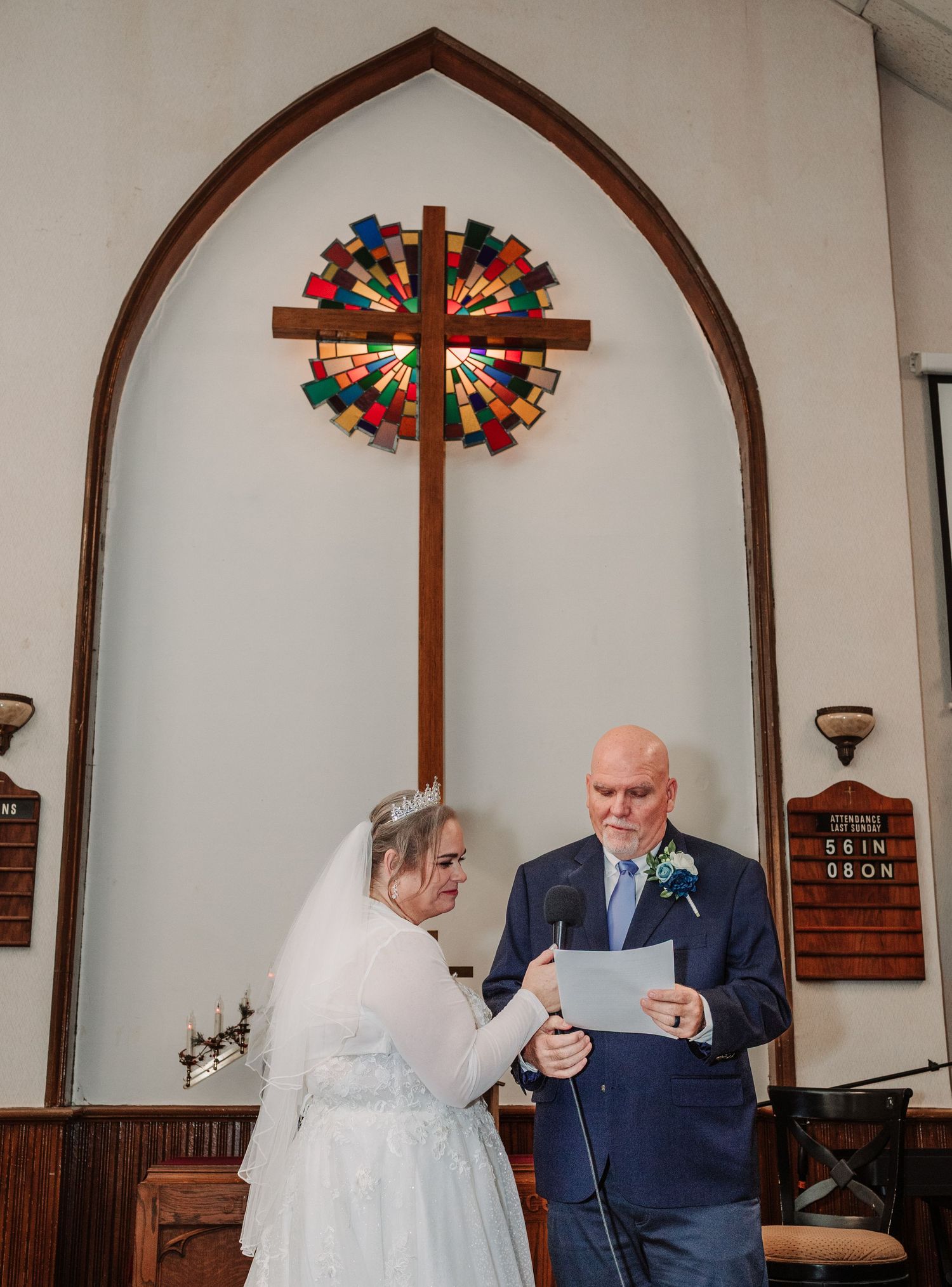 Bride and groom exchanging vows at church altar with stained glass cross.