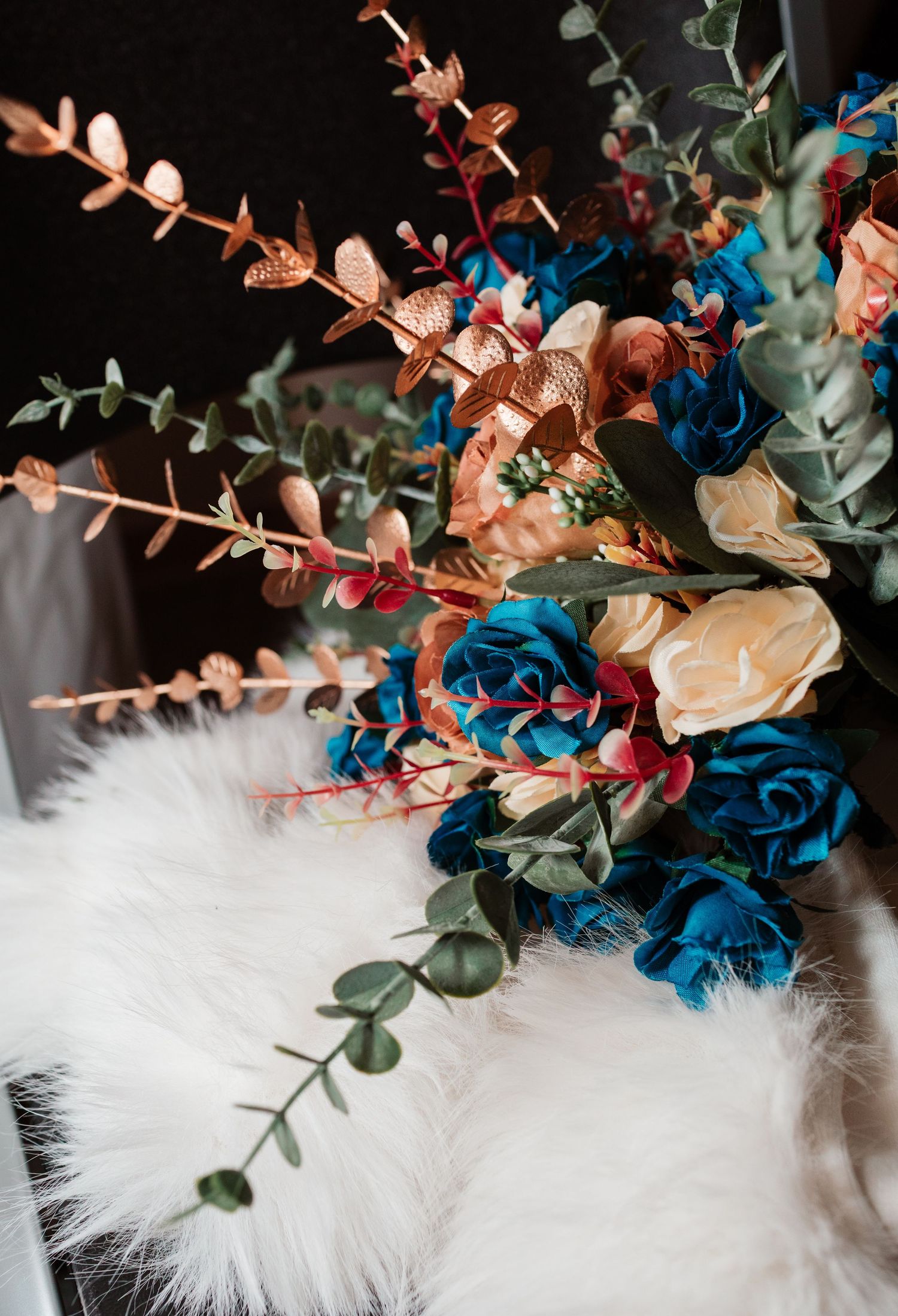 Wedding bouquet with blue roses, copper flowers, and eucalyptus on white fur.
