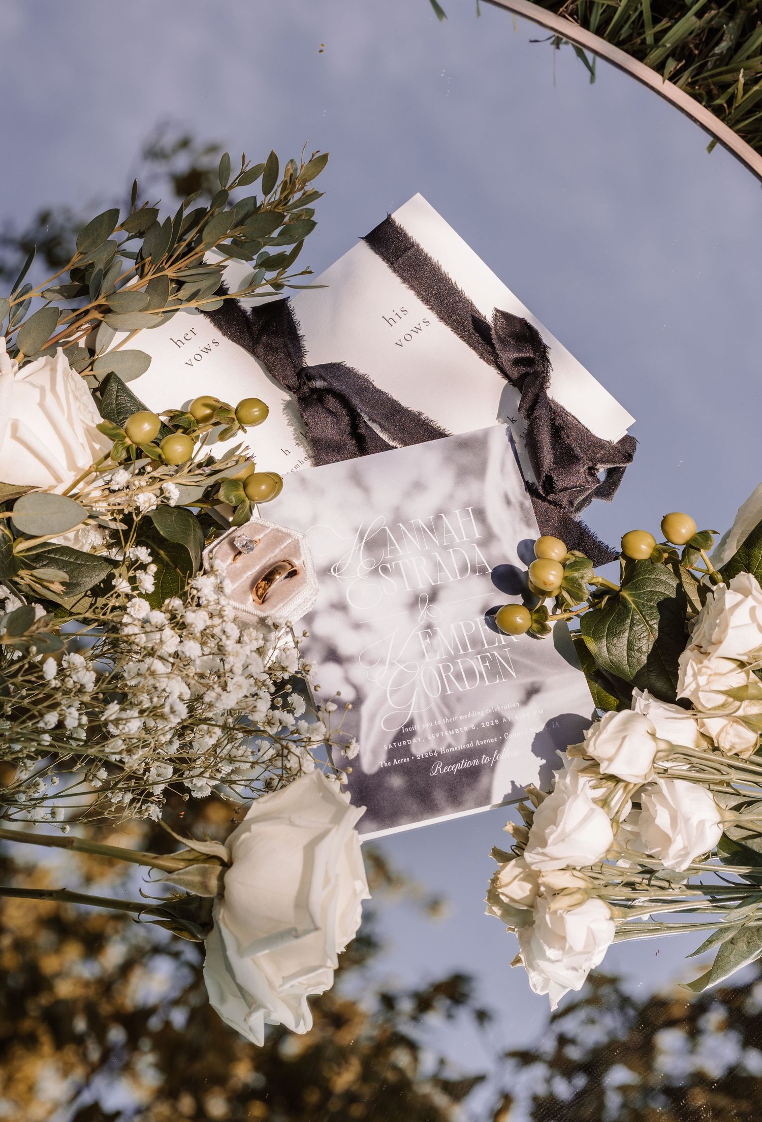 Elegant wedding ceremony arch with white roses, eucalyptus, and floral programs against a blue sky.
