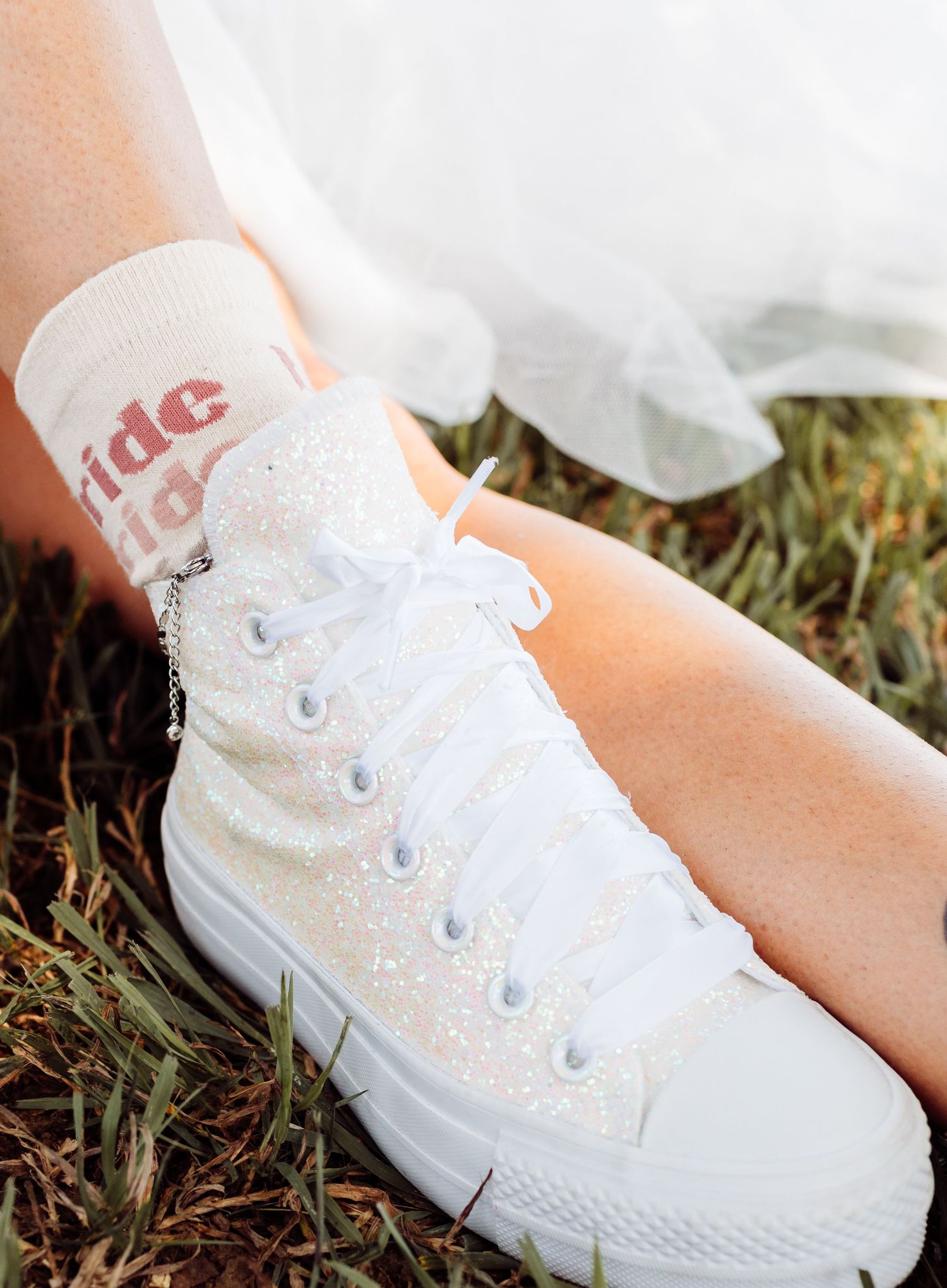 White glitter Converse high-top sneaker with ribbon laces and bride sock on a wedding day.