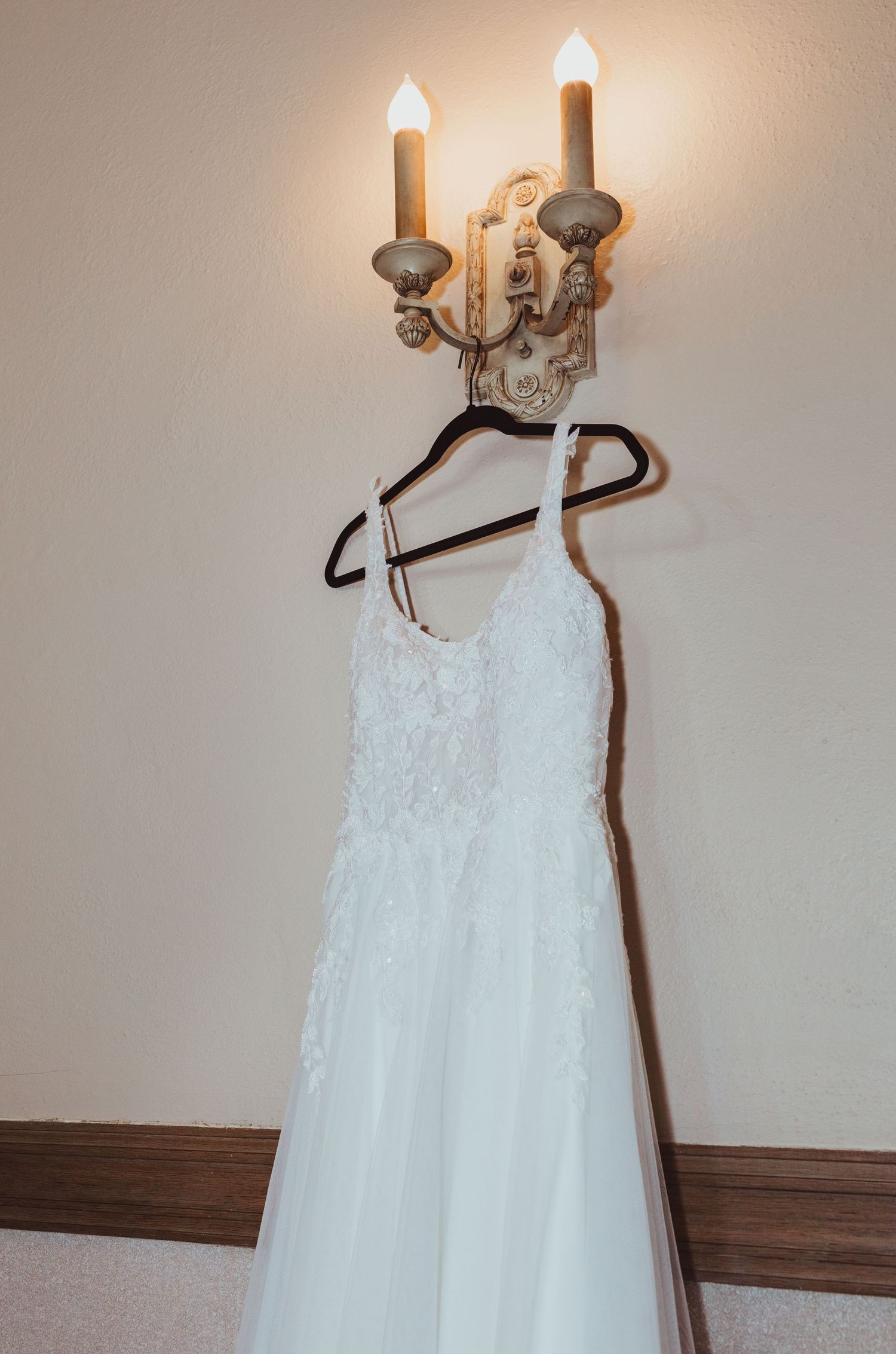White lace wedding dress hanging on a dark hanger from a vintage candle wall sconce.