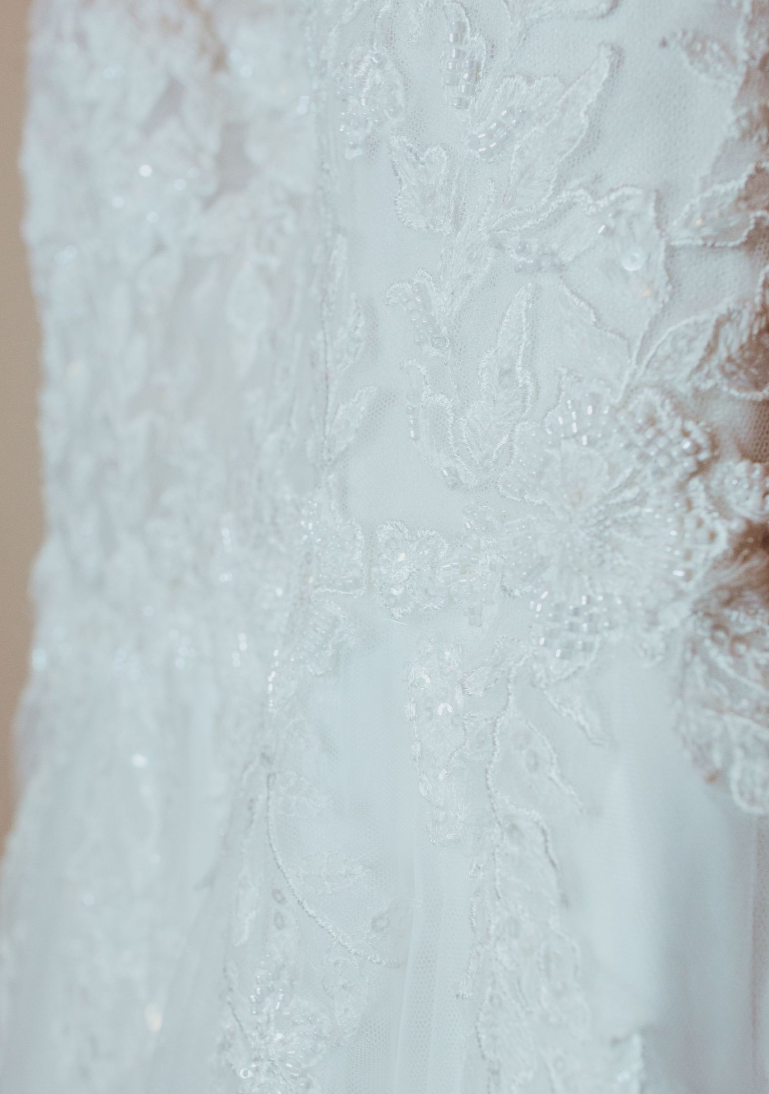 Close-up detail of intricate beaded floral lace embroidery on a white wedding dress.