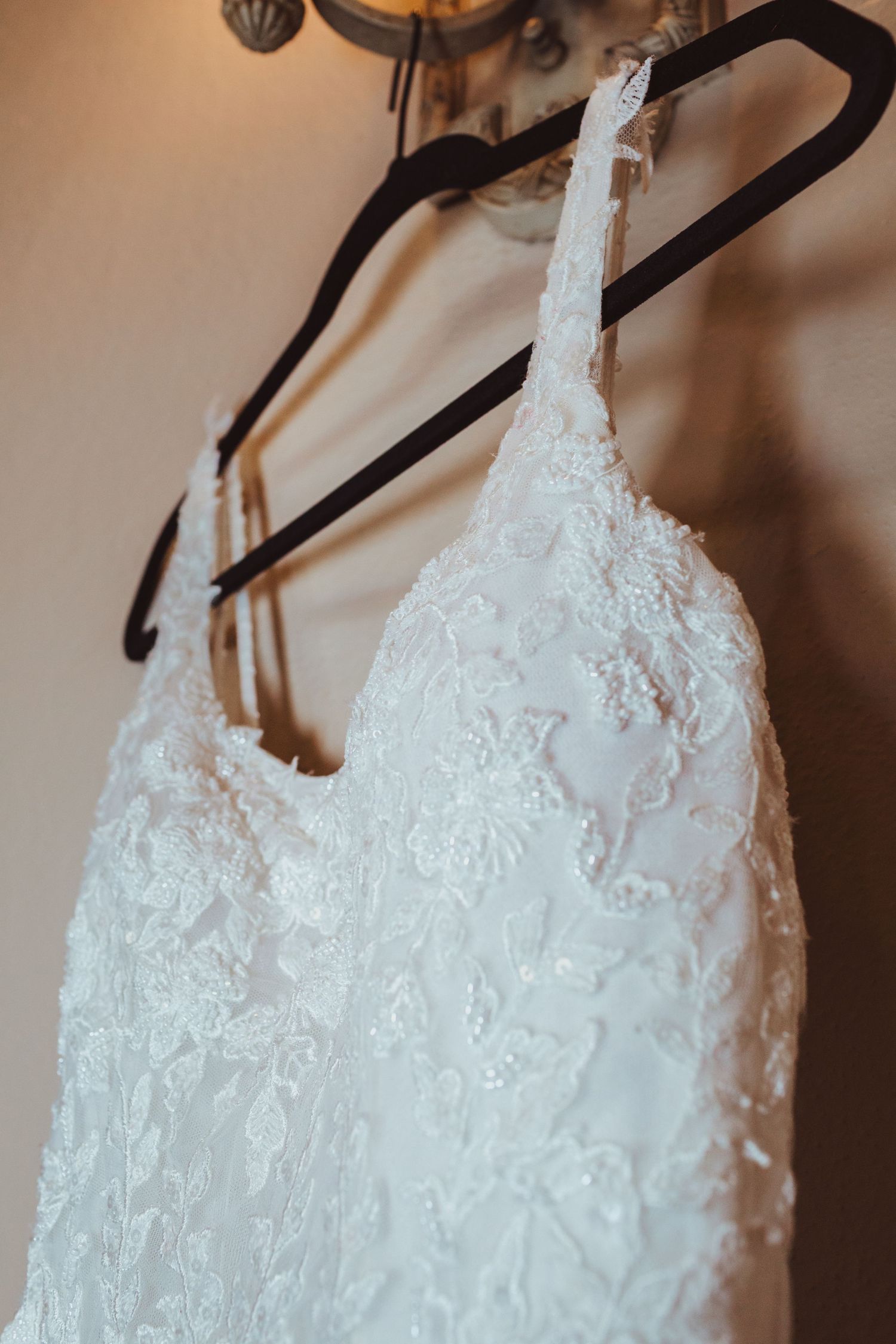Top detail of a white lace wedding gown with spaghetti straps on a velvet hanger.