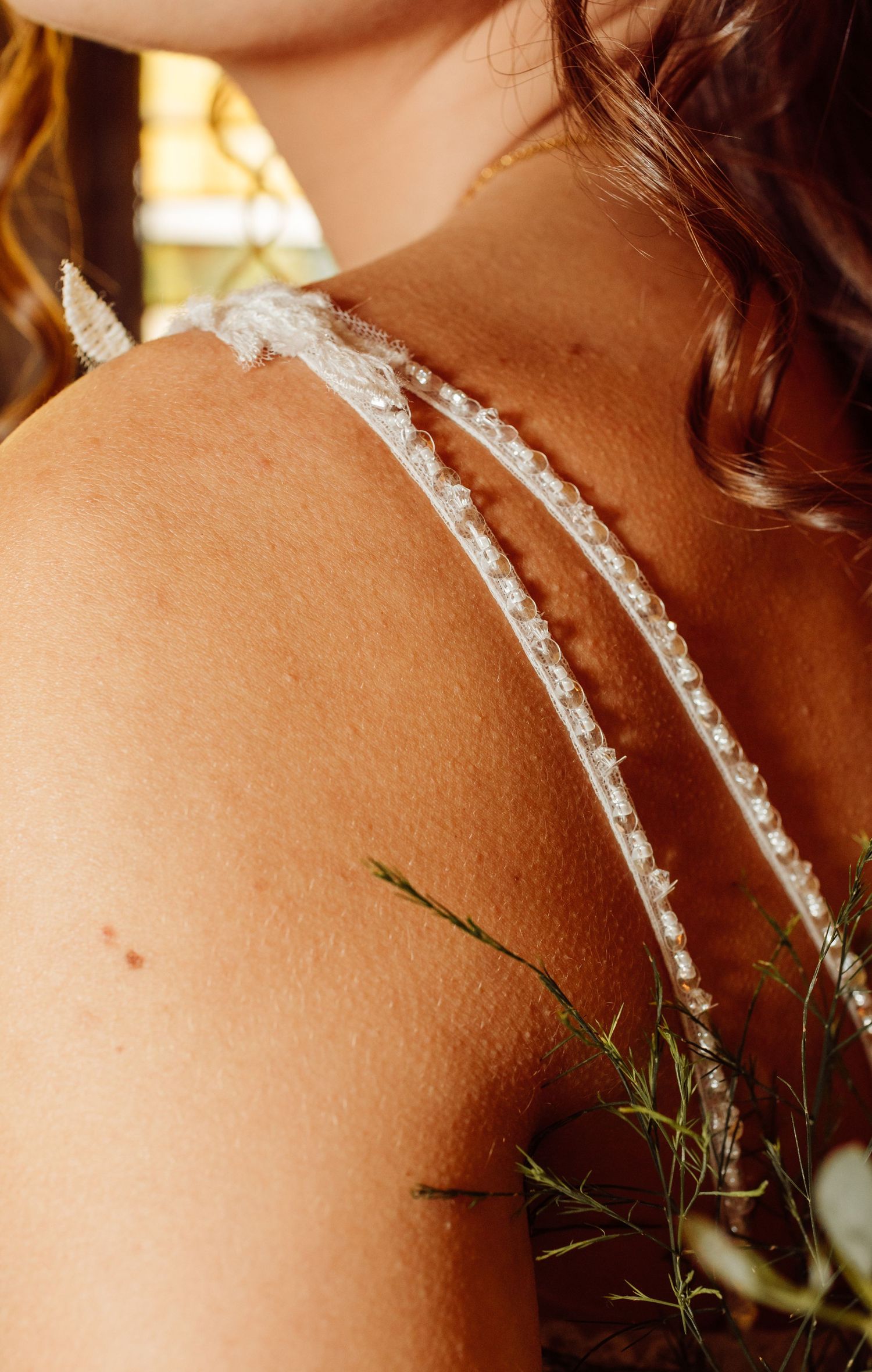 Close-up of delicate lace spaghetti straps on a bride's bare shoulder with floral detail.