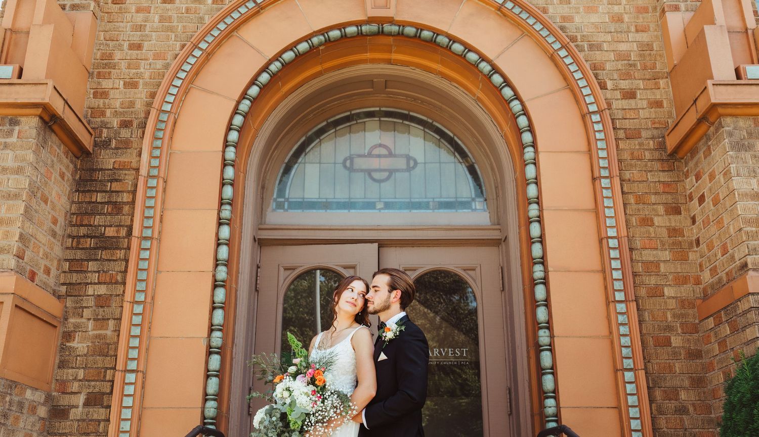 Newlywed couple shares kiss under decorative arched entrance of brick church after ceremony.