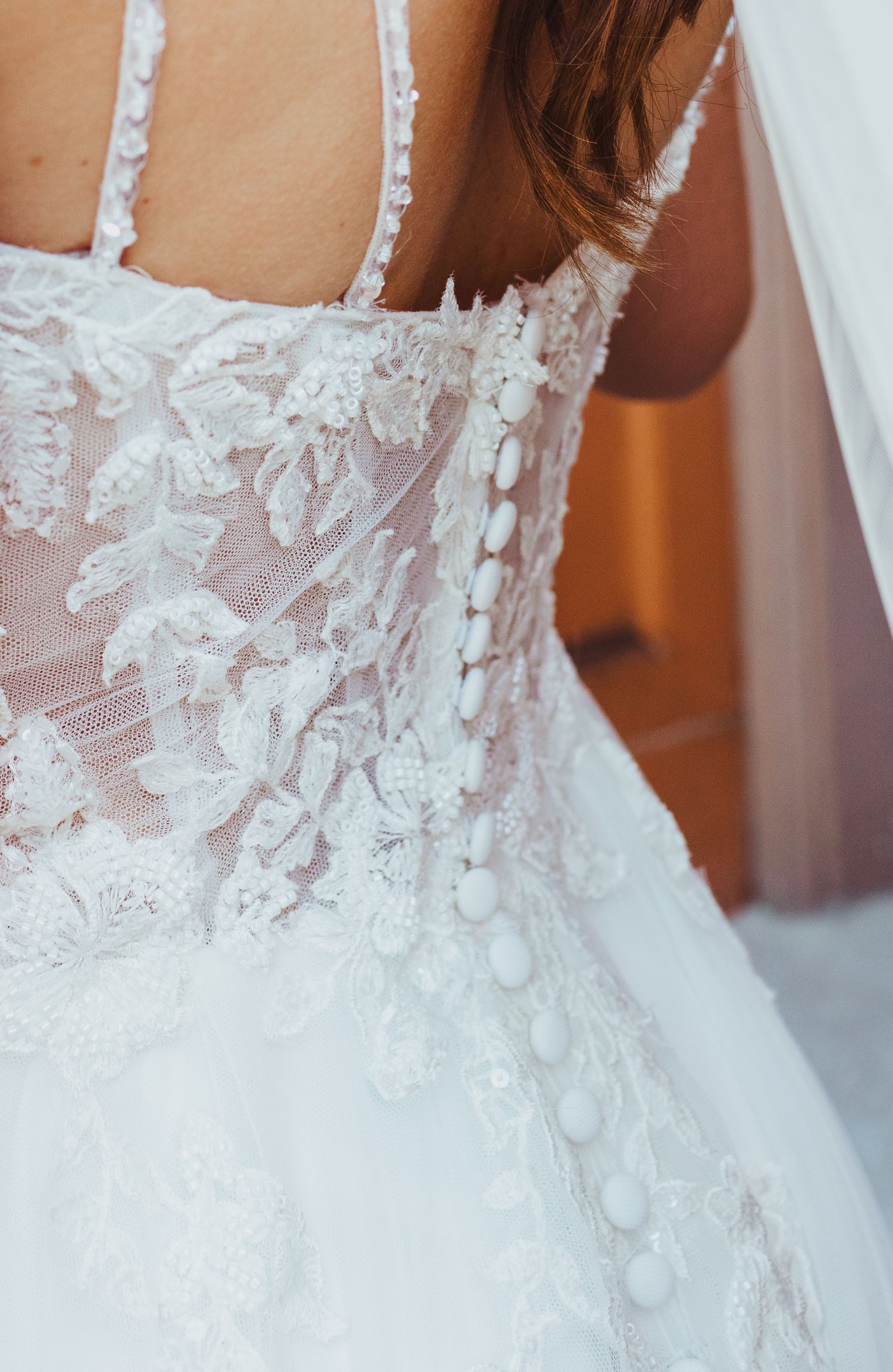 Close-up detail of intricate lace floral embroidery and button back of bridal wedding gown.