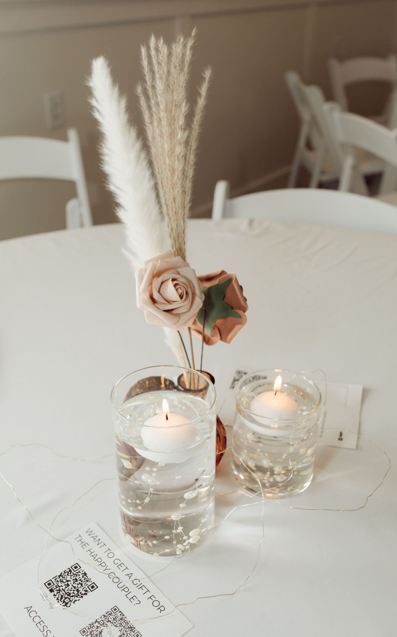 Elegant wedding table centerpiece with pampas grass, pink roses, and floating candles in glass vases.