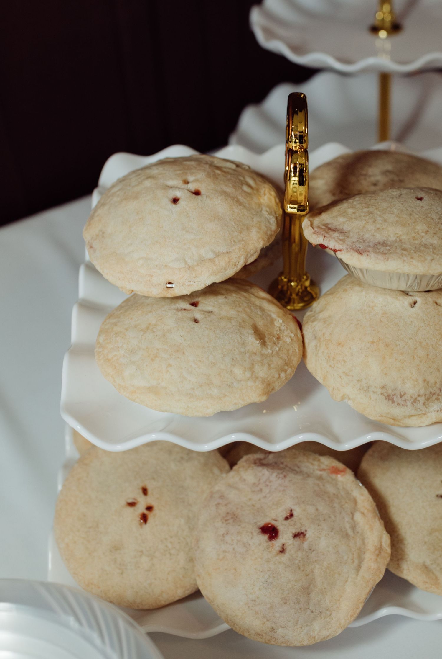 Freshly baked round cookies with red berry filling displayed on a white tiered serving stand with gold hardware.