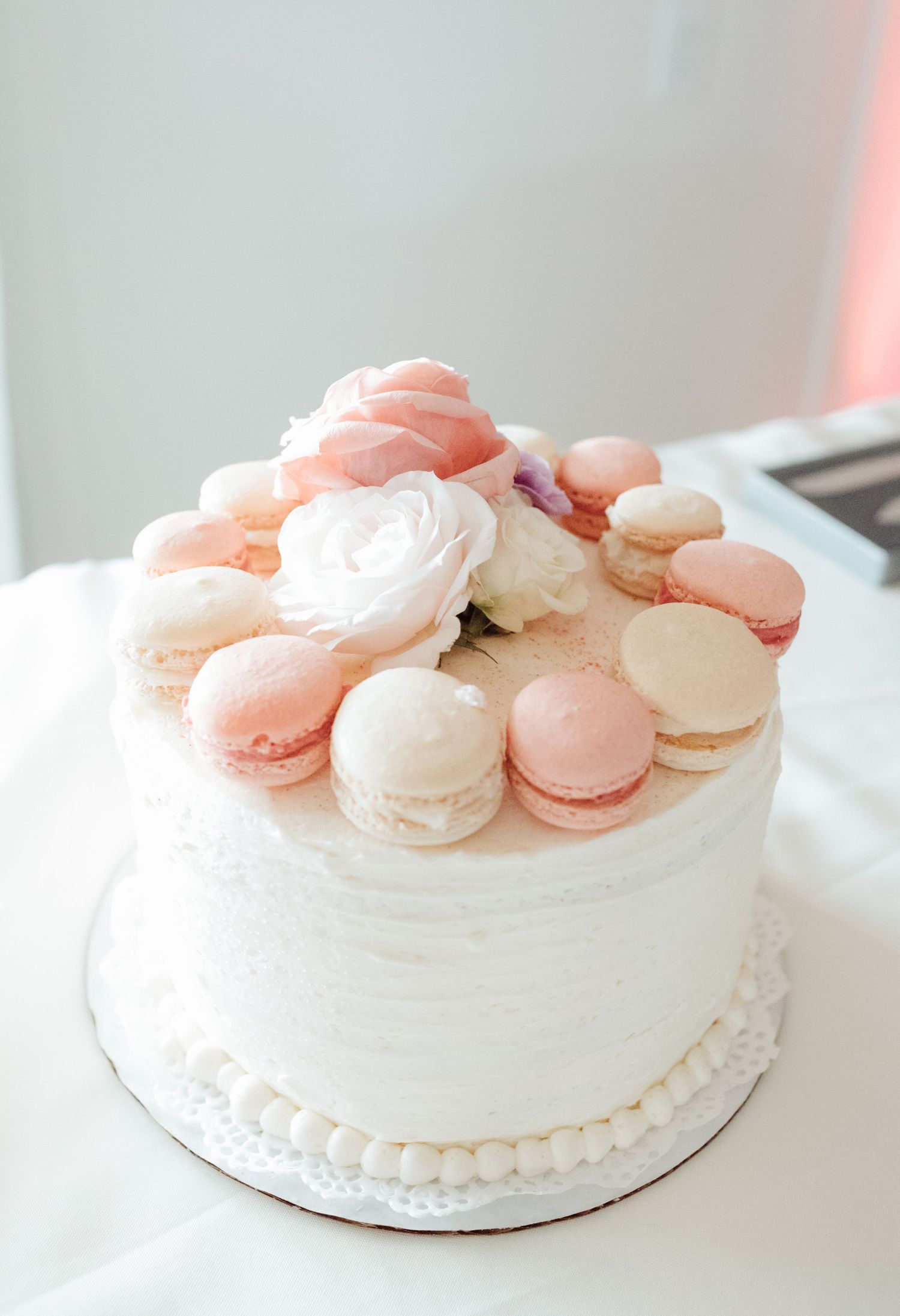 Elegant white wedding cake topped with pink and white macarons and fresh flowers.