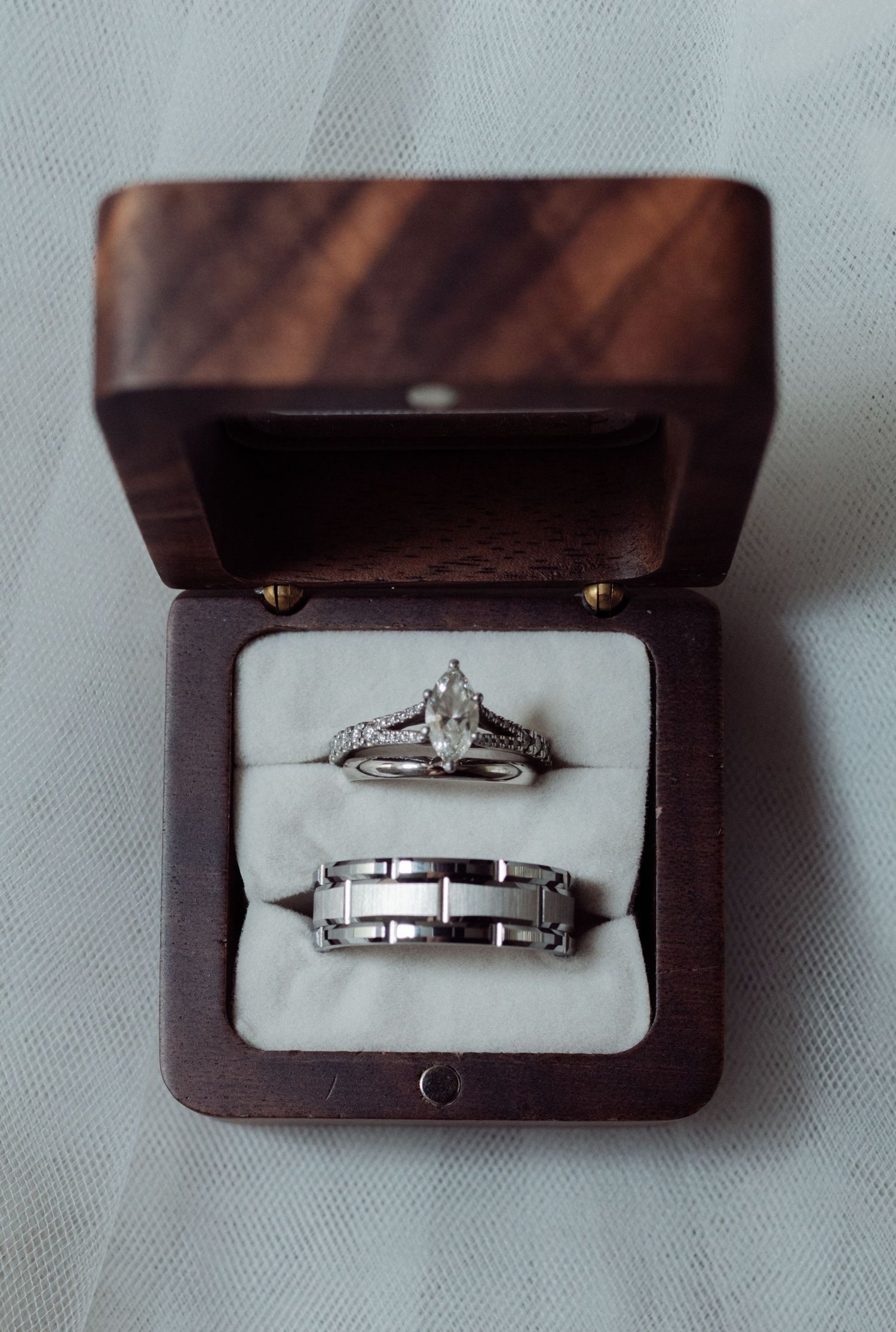 Wedding ring set displayed in a wooden box featuring a marquise diamond and silver band.