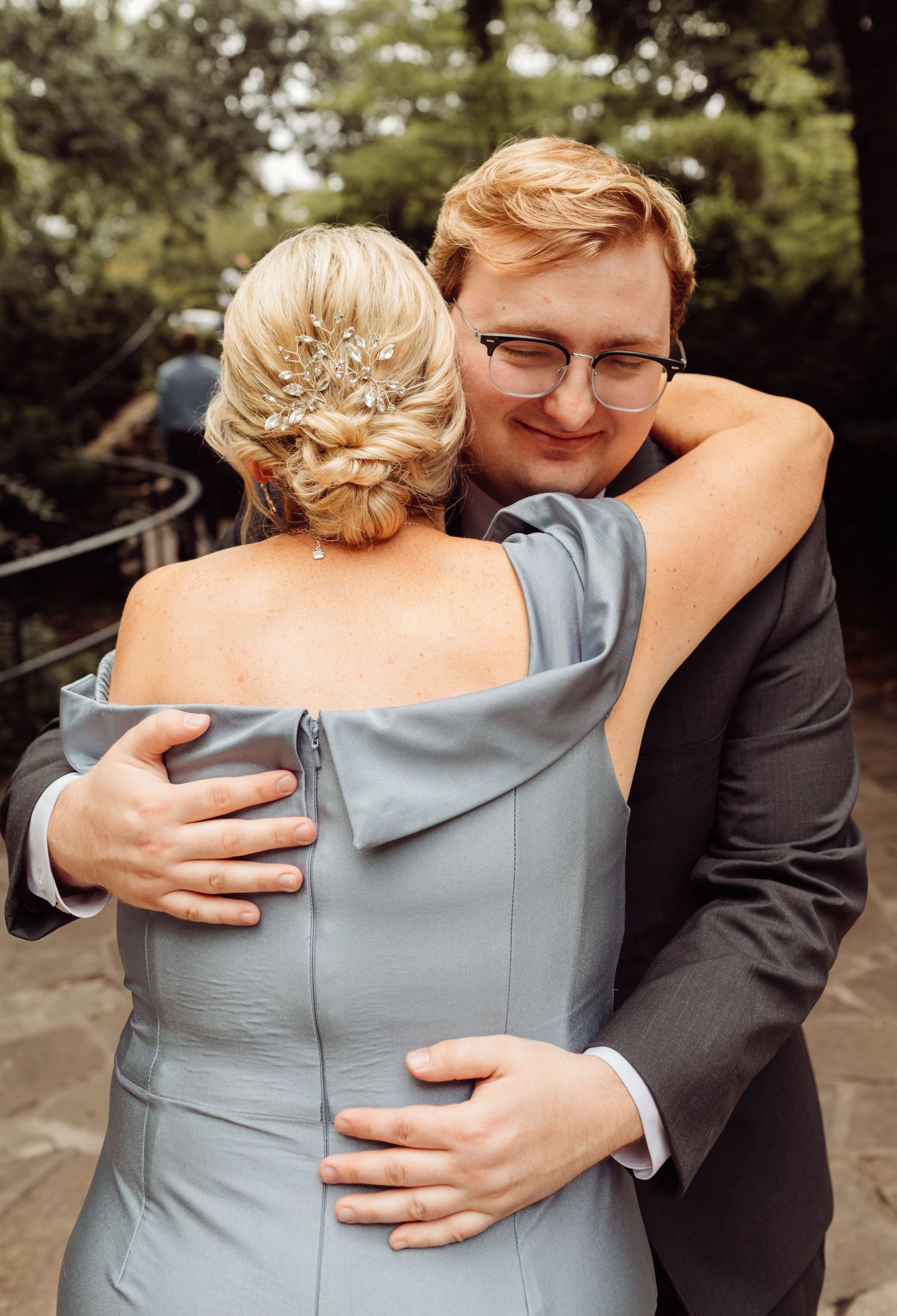 A groom in a suit shares a warm embrace with a woman in a blue off-shoulder dress.