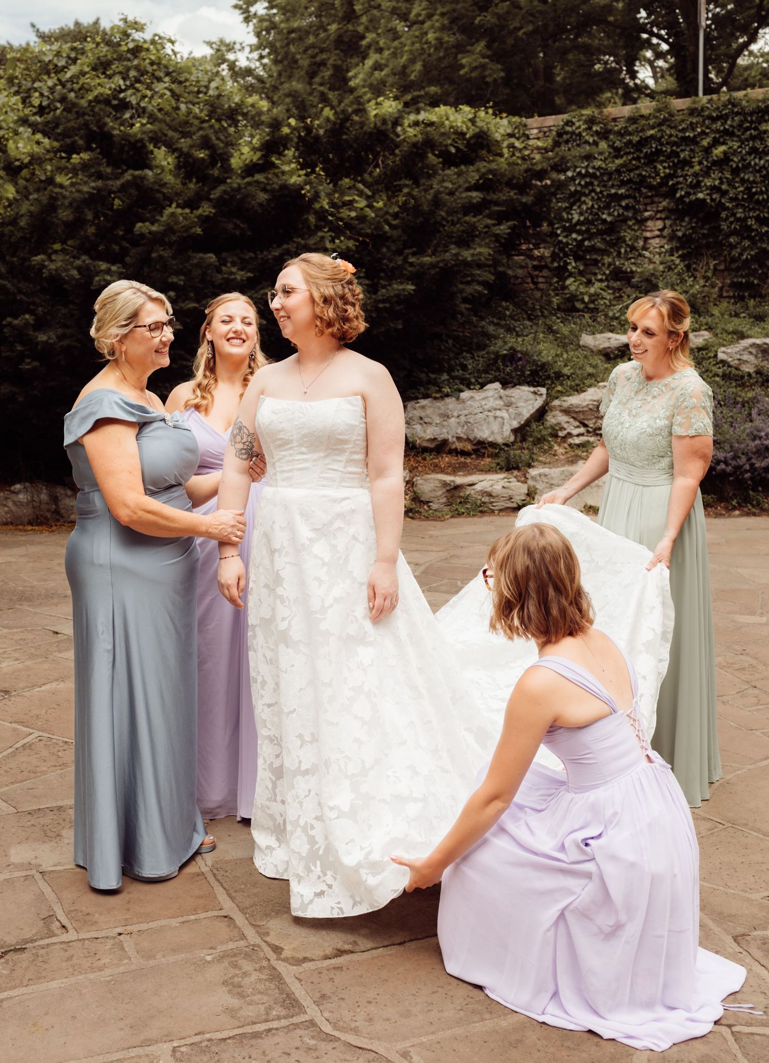 Bride surrounded by bridesmaids and mother in colorful gowns on a stone patio outdoors.