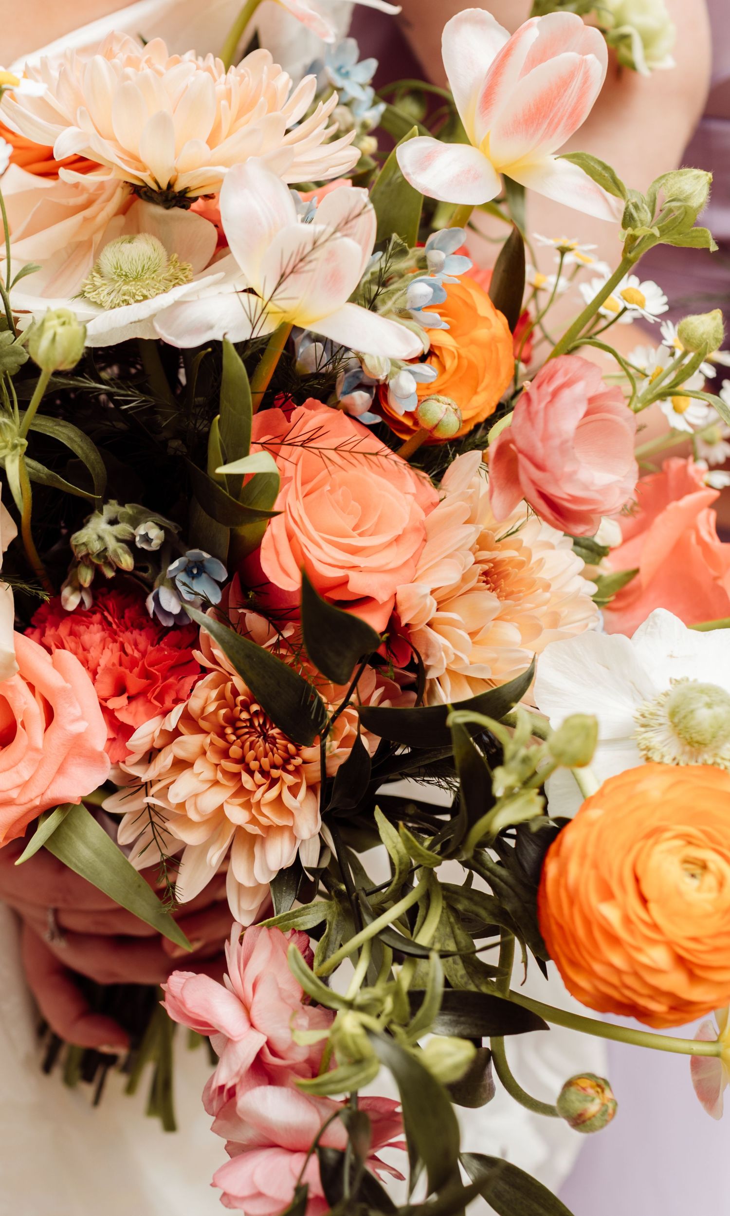 Close-up of vibrant wedding bouquet featuring orange ranunculus, pink roses, and white blooms.