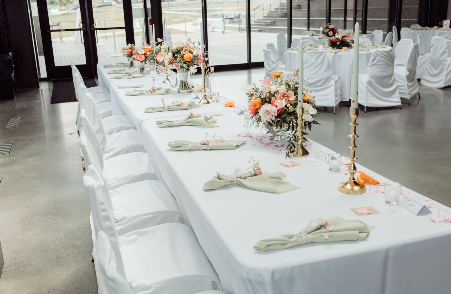 Elegant wedding reception table with white linens, folded napkins, gold candlesticks, and peach floral centerpieces.