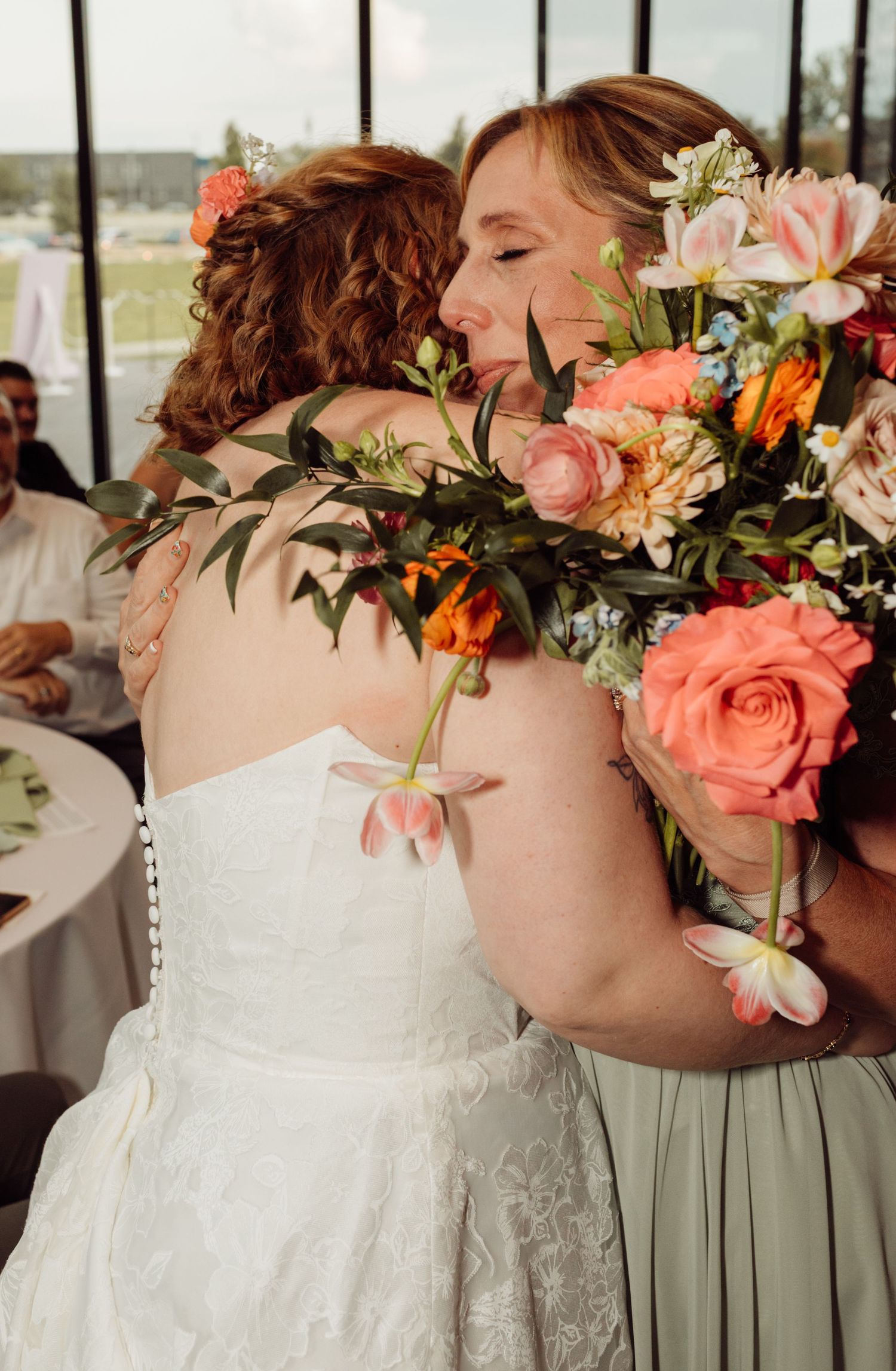 Bride sharing an emotional hug with a guest holding a colorful bouquet.