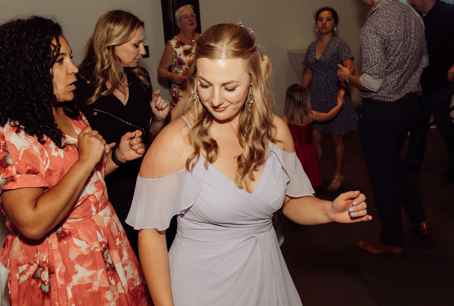 Two women in bridesmaid dresses dancing joyfully at a wedding reception.