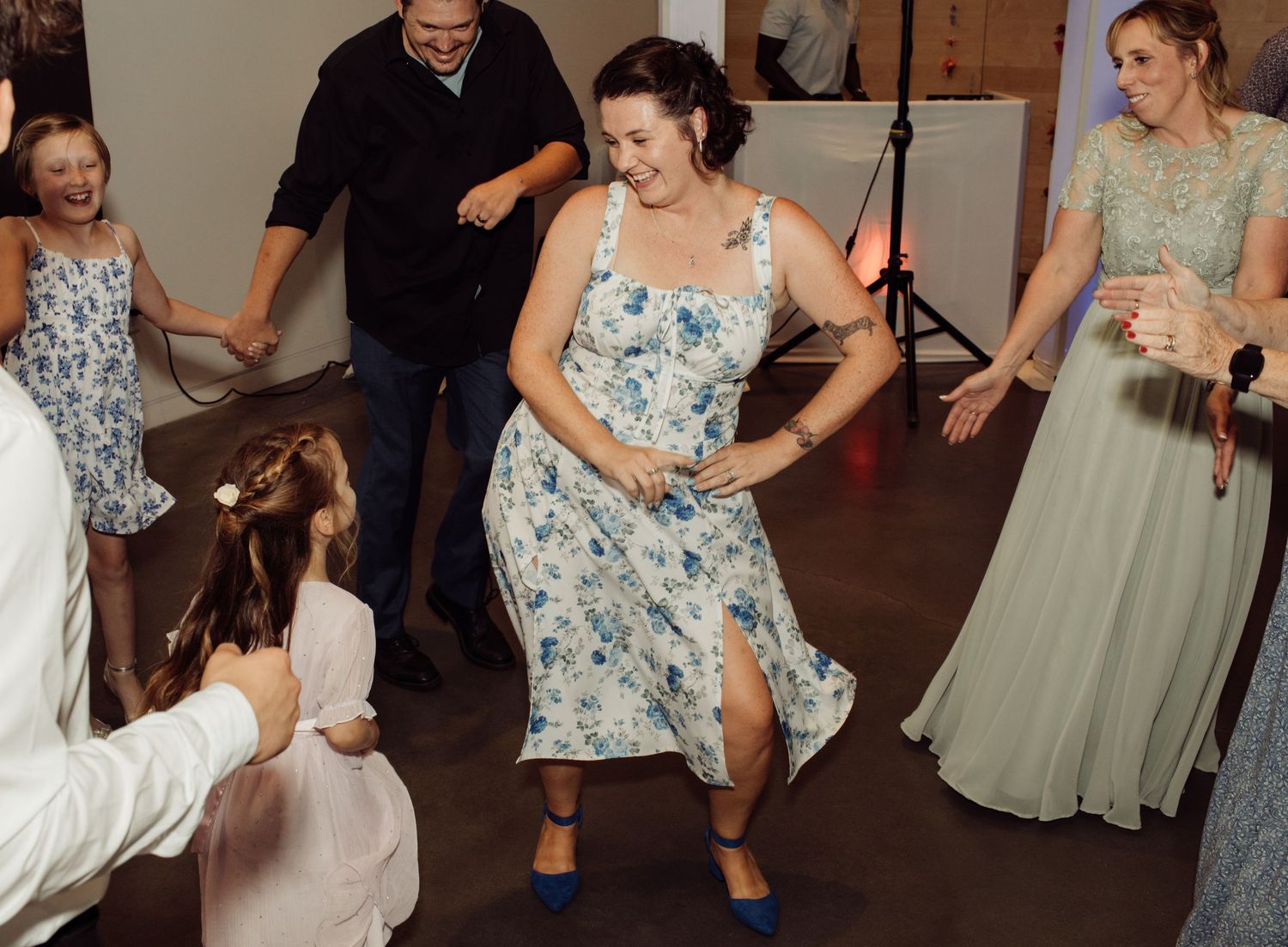 Woman in floral dress dancing energetically with a child at a wedding.