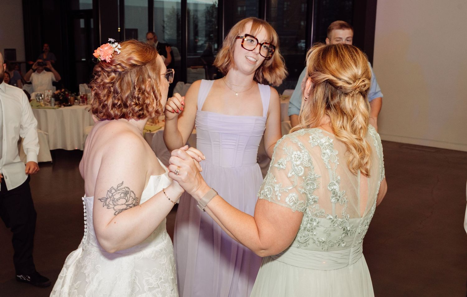 Bride dancing and holding hands with two guests at her wedding reception.