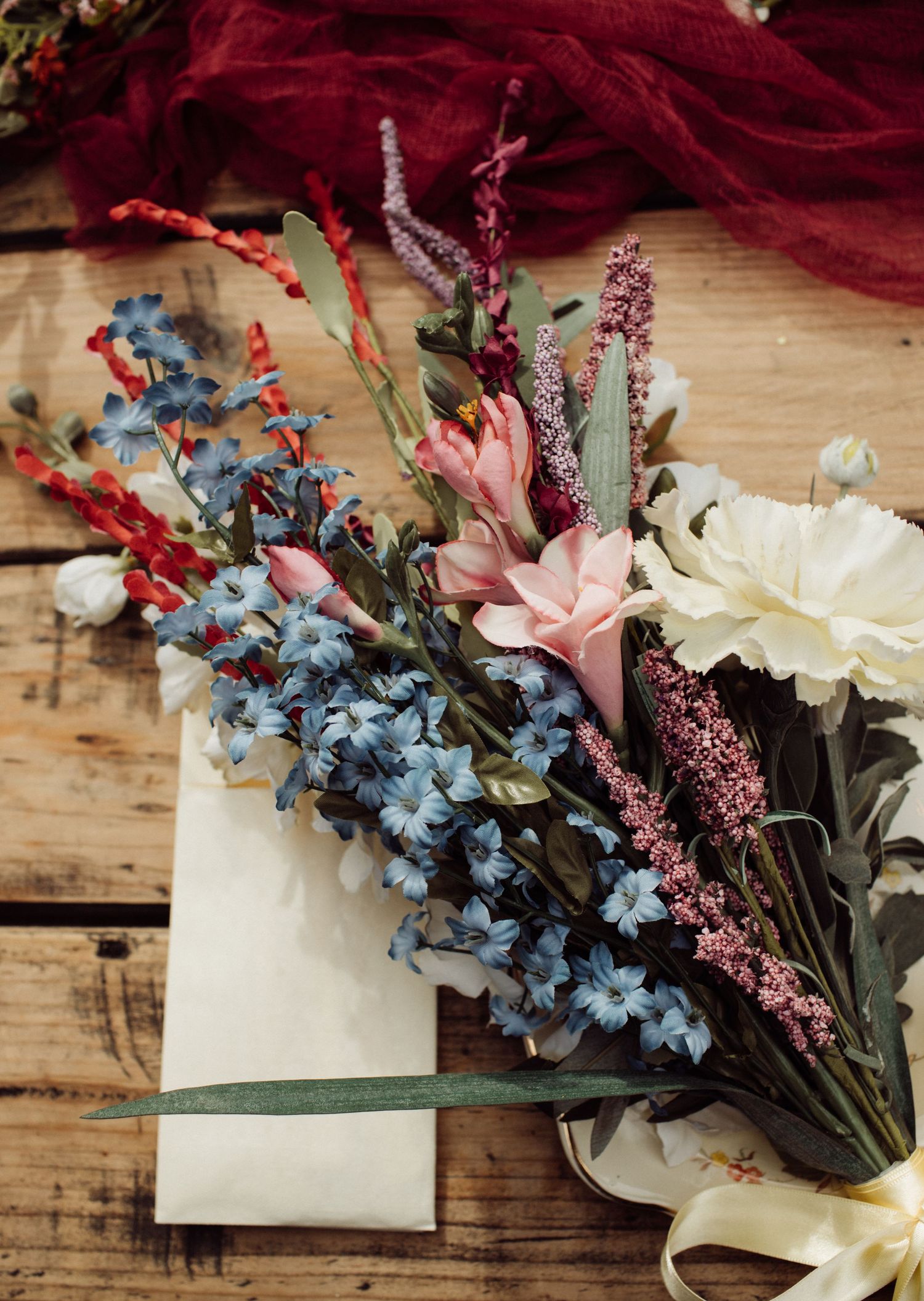 Colorful wedding bouquet with blue, red, pink, and white flowers arranged on rustic wooden surface.