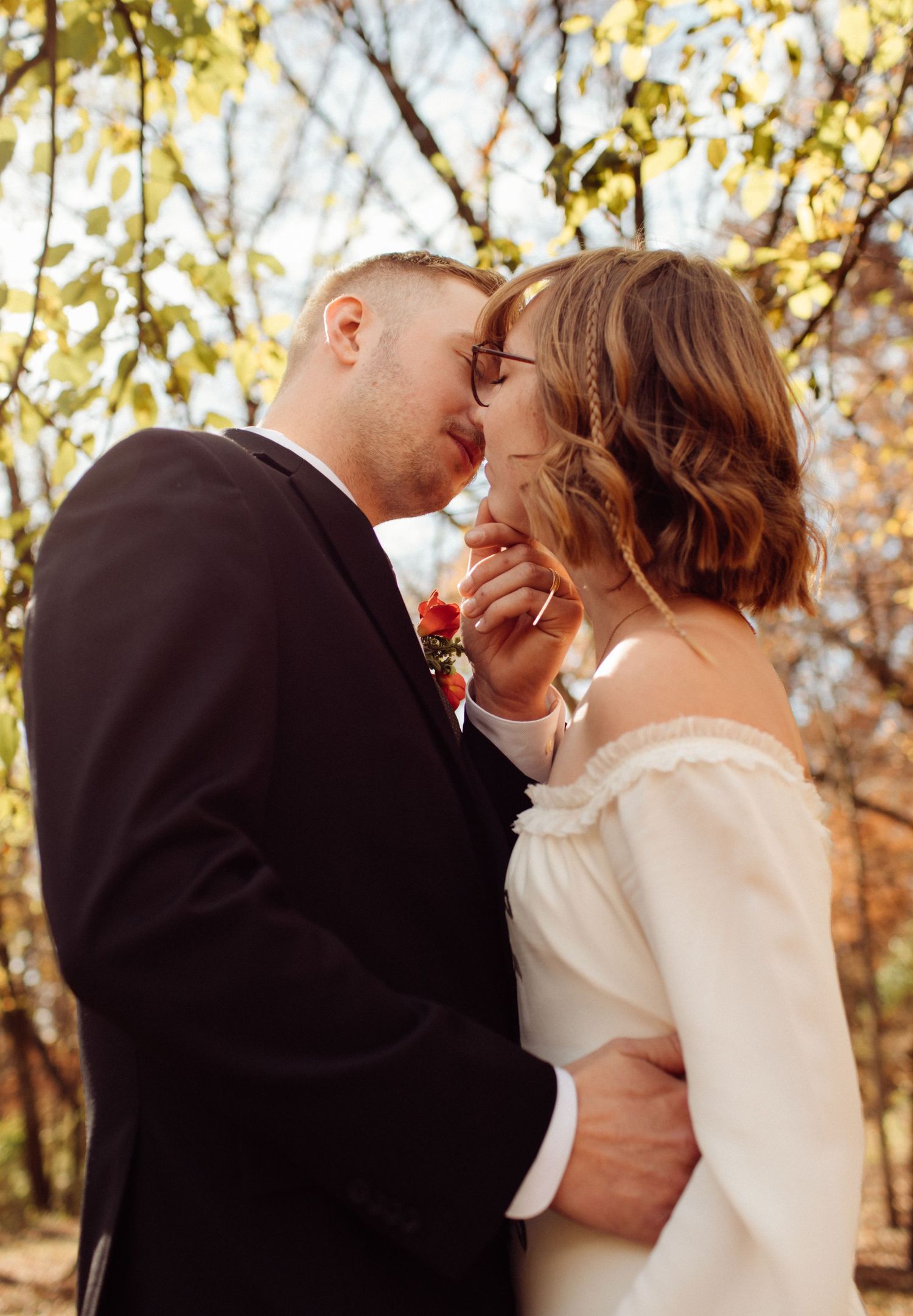 Bride and groom sharing intimate moment touching foreheads in golden autumn woodland setting.
