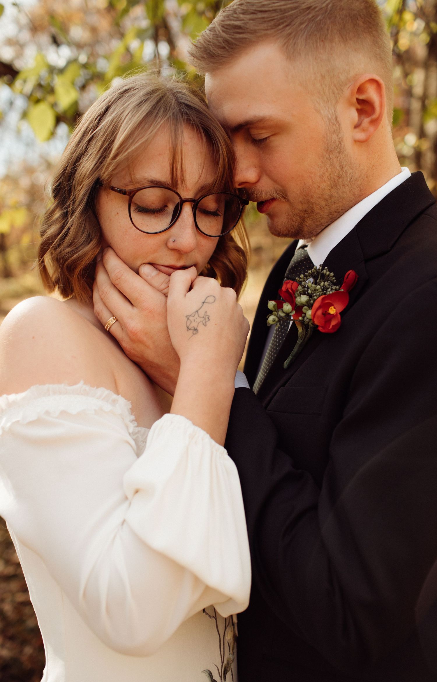 Emotional wedding couple moment with bride in off-shoulder white dress and groom in suit with red boutonniere.