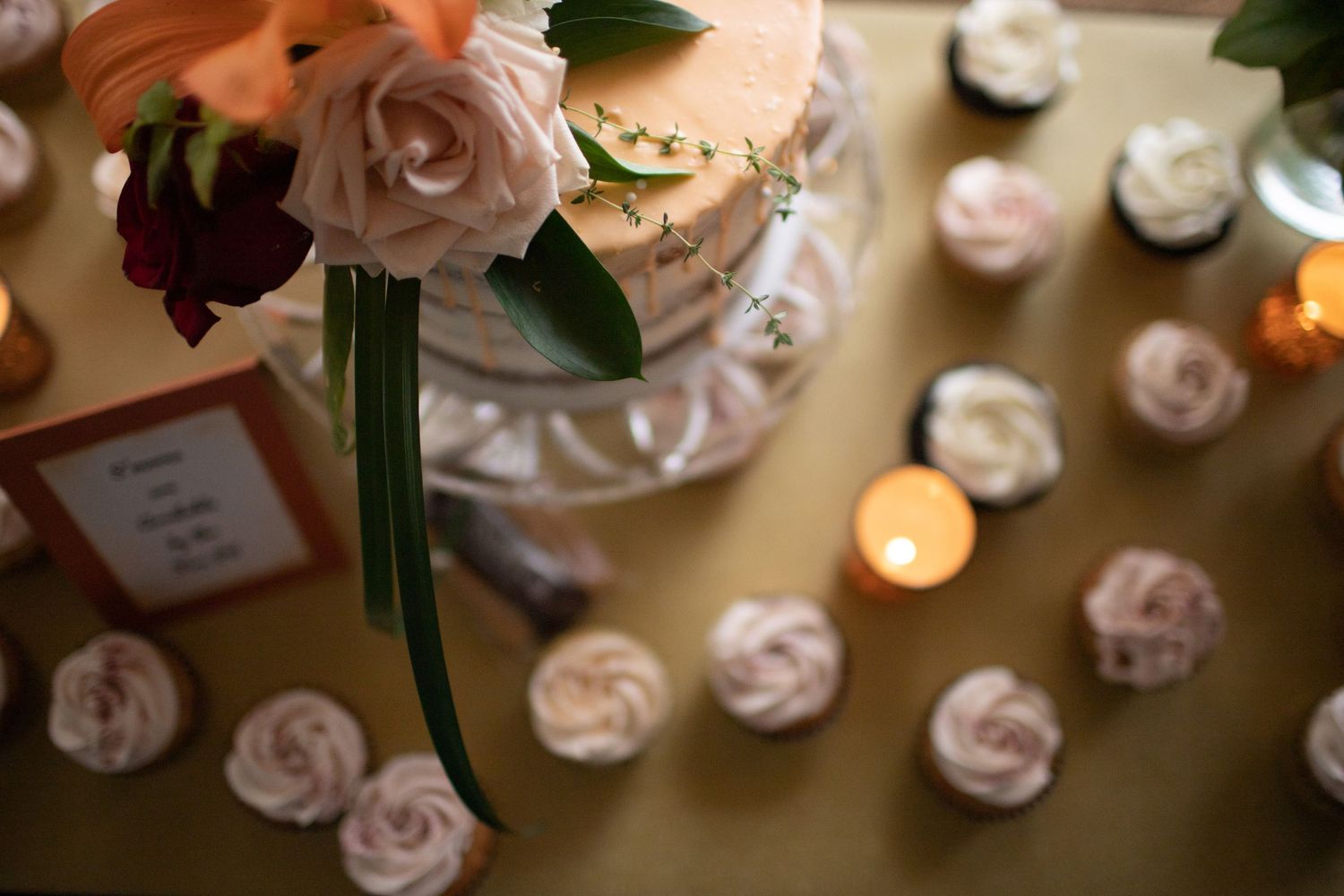 Wedding dessert table with floral-decorated cake, rose cupcakes, and glowing candles.