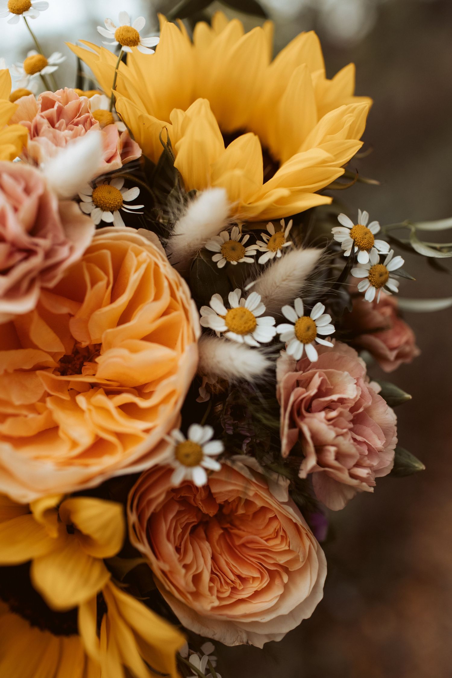 Autumn wedding bouquet with sunflowers, peach garden roses, pink carnations, and white daisies.