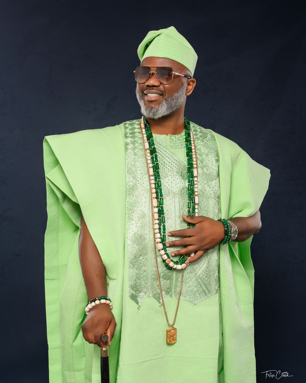 Someone wearing a bright lime green traditional African agbada outfit with beaded necklaces and a matching cap poses for a portrait.