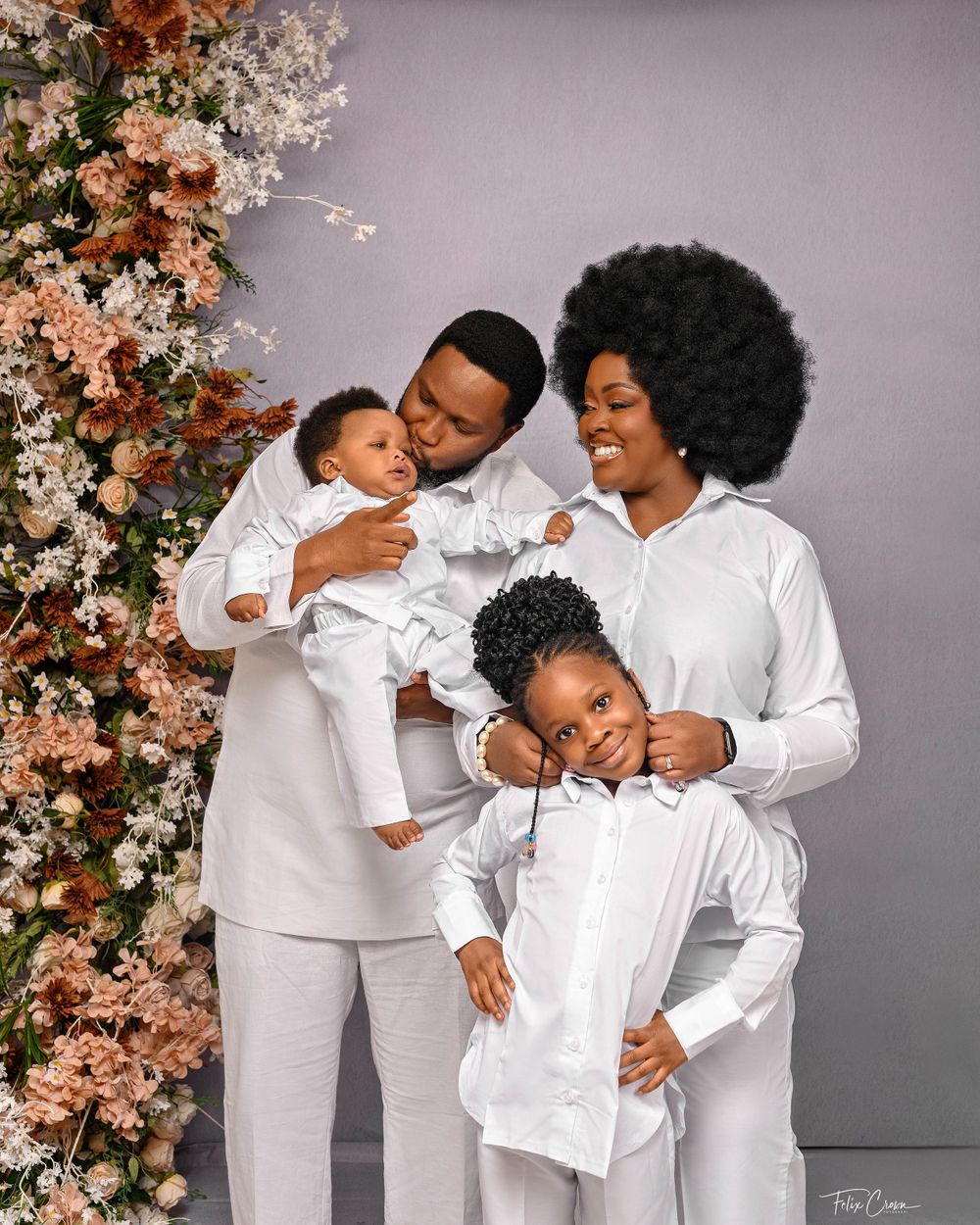 Family portrait in all white outfits posed against floral backdrop with peach blooms.